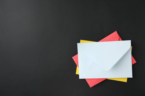 Stack of colorful paper envelopes on black background, top view. Space for text - Foto, immagini