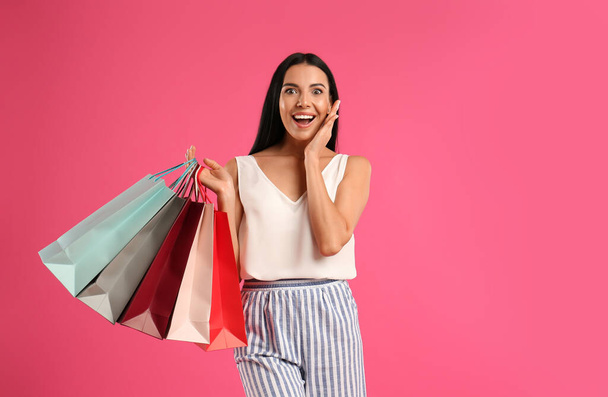 Beautiful young woman with paper shopping bags on pink background - Photo, Image