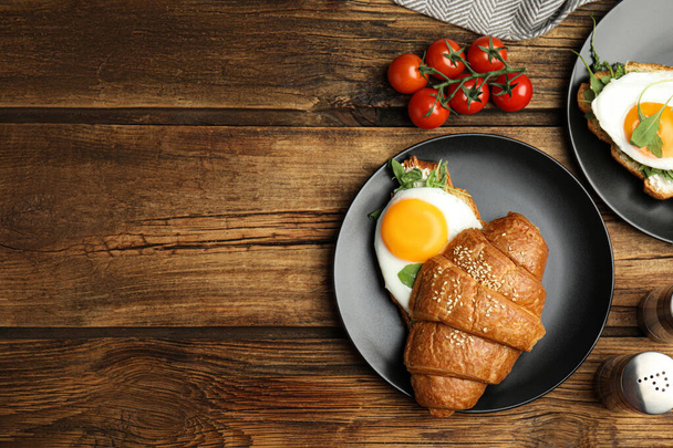 Delicious croissant with arugula and fried egg on wooden table, flat lay. Space for text - Foto, Bild