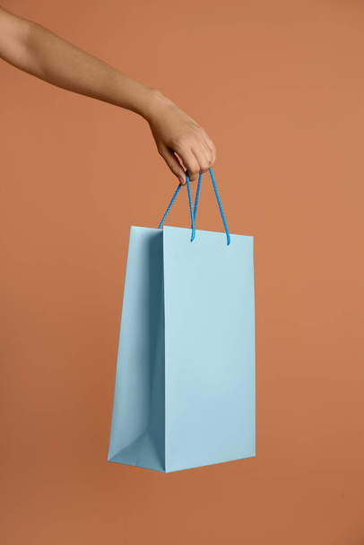Woman holding paper shopping bag on light brown background, closeup - Foto, afbeelding
