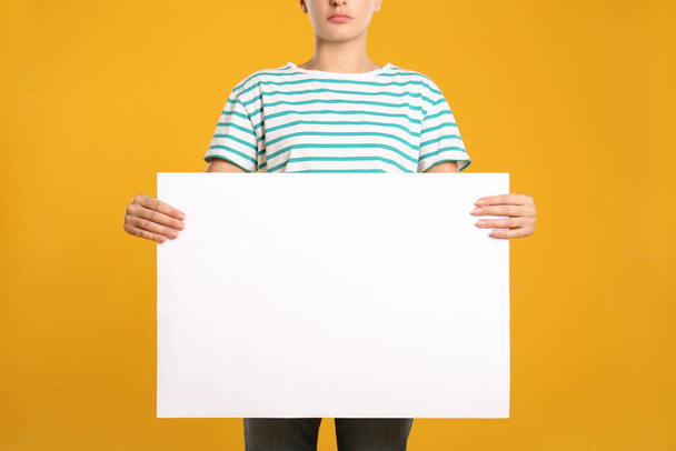 Woman holding white blank poster on yellow background, closeup. Mockup for design - Foto, afbeelding