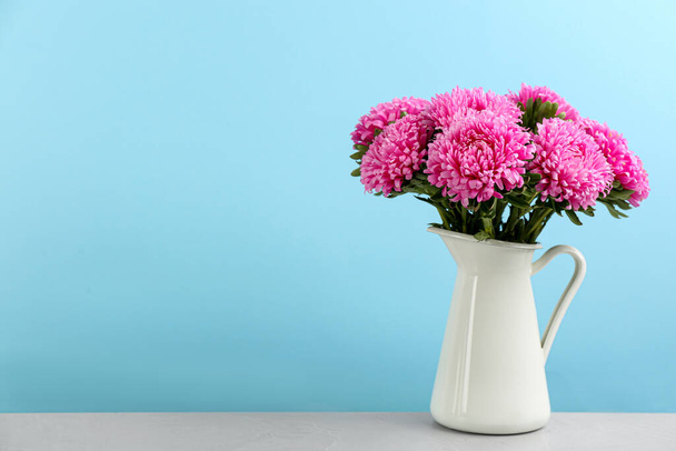 Beautiful asters in jug on table against light blue background, space for text. Autumn flowers - Fotoğraf, Görsel