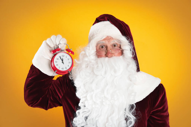 Santa Claus holding alarm clock on yellow background. Christmas countdown - Foto, Imagen