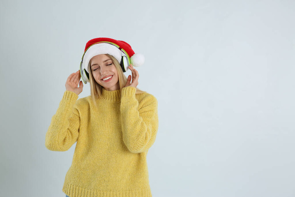Happy woman with headphones on light grey background, space for text. Christmas music - Foto, afbeelding