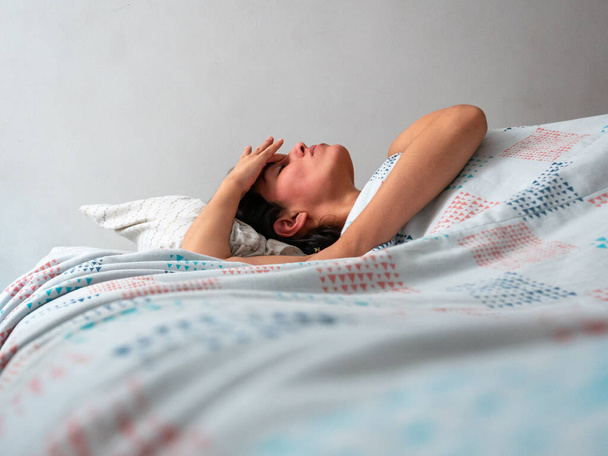 Junge Frau mit braunem Haar berührt ihr Gesicht beim Aufwachen im Bett - Foto, Bild