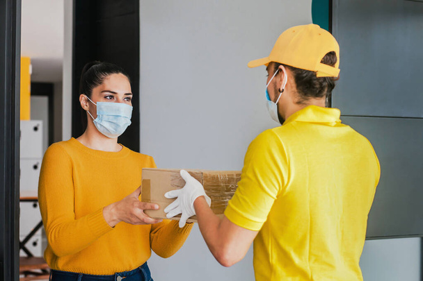 Latijnse bezorger met masker die een kartonnen doos vasthoudt en draagt bij een quarantaine coronavirus pandemie - Foto, afbeelding