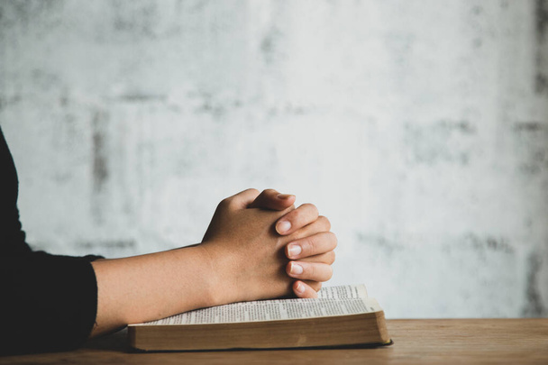 Γυναίκα με Αγία Γραφή προσεύχεται, τα χέρια ενωμένα στη Βίβλο της σε ξύλινο τραπέζι. - Φωτογραφία, εικόνα