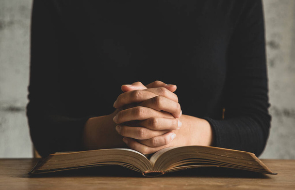 Γυναίκα με Αγία Γραφή προσεύχεται, τα χέρια ενωμένα στη Βίβλο της σε ξύλινο τραπέζι. - Φωτογραφία, εικόνα