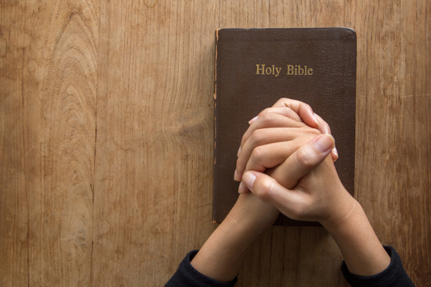 Mujer con la Biblia rezando, las manos juntas en su Biblia sobre una mesa de madera. - Foto, imagen