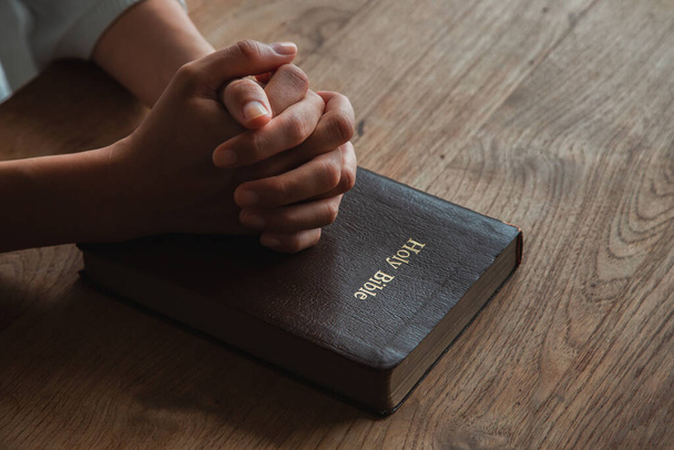 Mulher com a Bíblia orando, mãos apertadas juntas em sua Bíblia na mesa de madeira. - Foto, Imagem