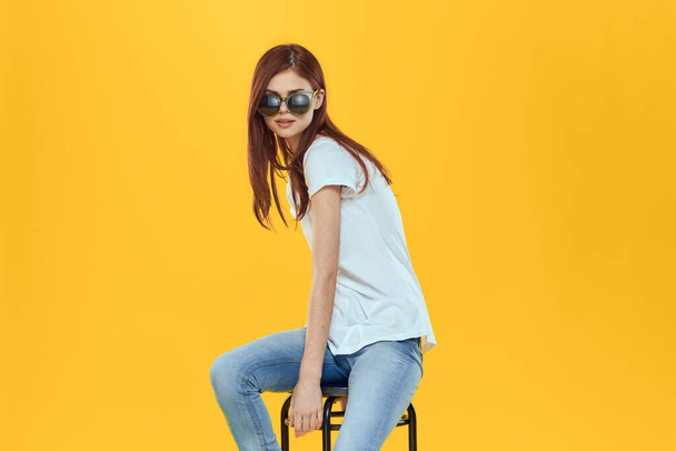 Csinos nő ül egy széken visel napszemüveg sárga háttér életmód - Fotó, kép