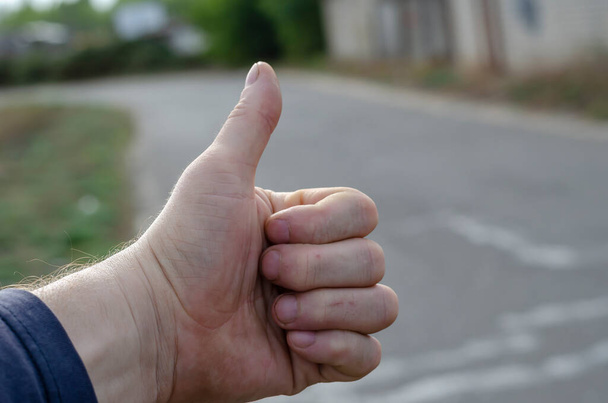 Primo piano di una palma maschile vuota con un gesto da autostoppista. La mano di un uomo è tesa in lontananza sulla strada. Mano di un viaggiatore adulto. - Foto, immagini