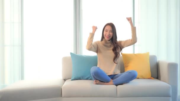 metraje de hermosa joven asiática mujer celebrando en sofá - Metraje, vídeo