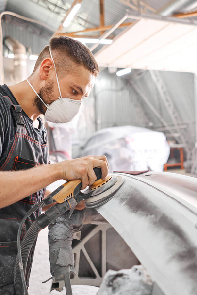 The mechanic works with a grinding tool. Sanding of car elements. Garage painting car service. Repairing car section after the accident. - Photo, Image