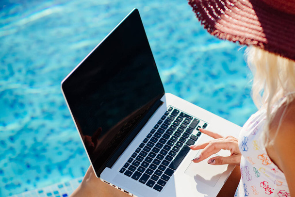 Frau benutzt Laptop und arbeitet aus der Ferne in Schwimmbadnähe - Foto, Bild