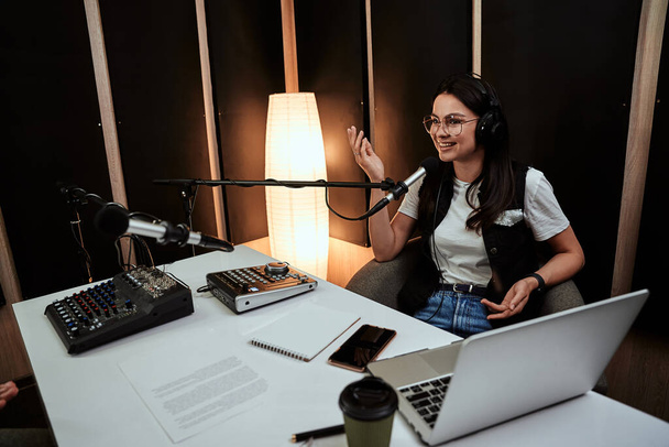 Portret van aantrekkelijke jonge vrouwelijke radio host op zoek vrolijk tijdens het spreken in de microfoon, het modereren van een live show - Foto, afbeelding