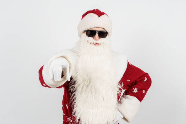 Christmas and New Years concept. Santa Claus in dark glasses points his finger towards the camera. Isolated background - Fotoğraf, Görsel