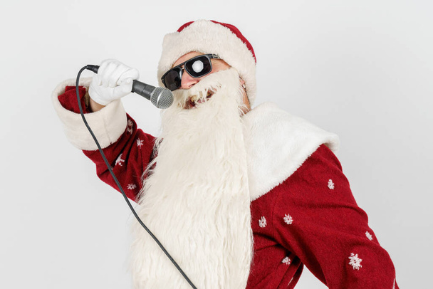 Holidays and christmas concept. Santa Claus sings with a microphone in his hand. Isolated on white - Foto, afbeelding