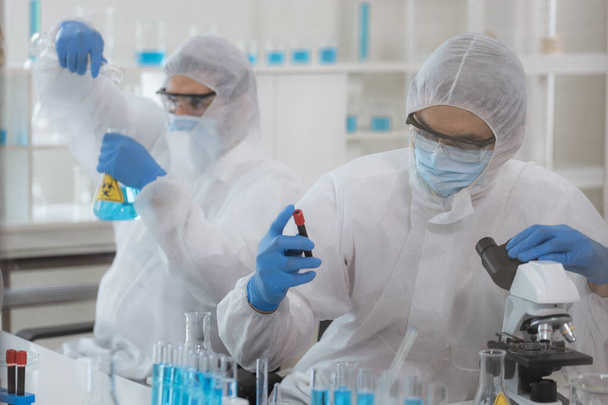 Onderzoekers in de gezondheidszorg werken in het laboratorium voor biowetenschappen. Mannelijke onderzoeker en supervisor die microscoopdia 's voorbereiden en analyseren in het onderzoekslaboratorium. Uitvinding van het coronavirusvaccin - Foto, afbeelding