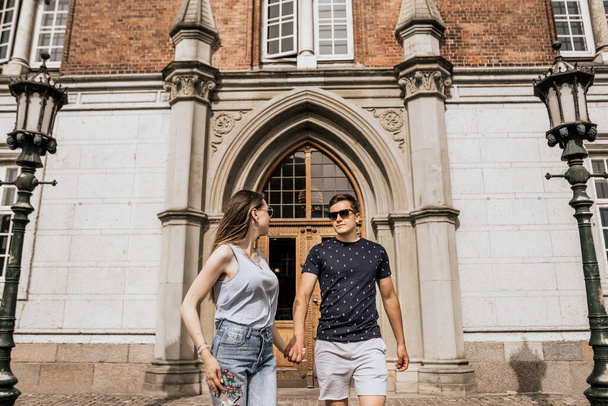 Horizontal photo of romantic couple stand hold hands and look to each other. Happy man and woman on building background - Фото, зображення
