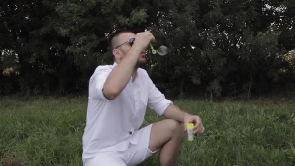 Fiatal apa buborékokat fúj boldog gyermekének a parkban. - Felvétel, videó