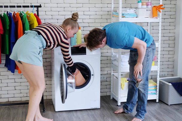 Lächelndes junges kaukasisches Liebespaar, das Mann und Frau liebt, holt die Wäsche in der Waschmaschine zusammen in der Waschküche ab. Lebensstil von Familie und Verheirateten im Ferienkonzept - Foto, Bild