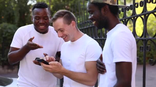 Üç çok ırklı öğrenci birbirleriyle iletişim kurar, telefona bakar ve gülerler. - Video, Çekim