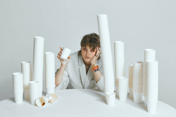 Tired female with lots of paper cups for coffee on gray studio background - Photo, image