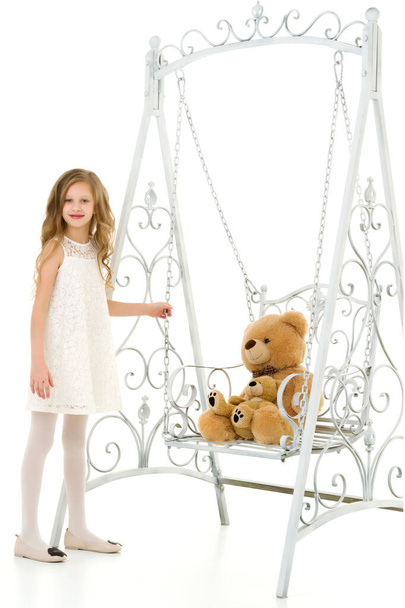 Blonde Girl in Elegant White Dress Swinging Her Teddy Bear on Swing. - Foto, Imagen