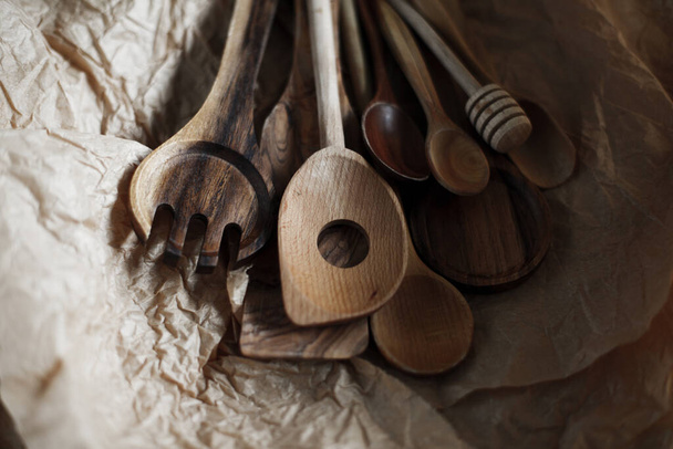 Wooden spoons of various shapes and purposes lie on crumpled craft paper. Kitchen utensils on a dark background - Valokuva, kuva