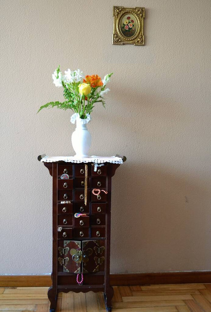 Sieraden ladekast met daarop een vaas bloemen en een foto van bloemen op de muur erachter - Foto, afbeelding