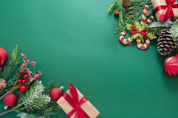 Christmas green background with winter decorations, gift boxes, fir branches, pine cones and red baubles. Copy space. - 写真・画像
