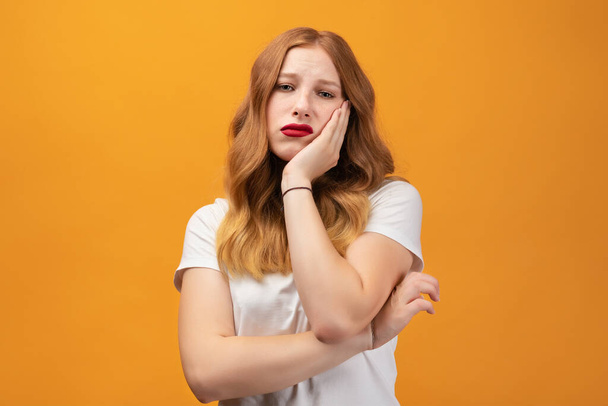 Photo of tired girl with wavy redhead, wearing white t-shirt covers face hand, feels fatigue, needs good rest, has sleepy expression, isolated on yellow background. Weariness and people - Photo, Image