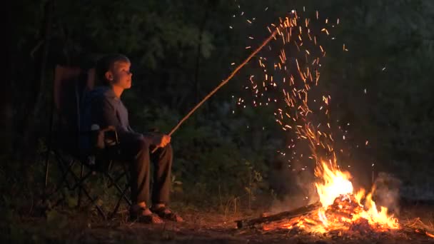 Child boy sitting near capming fire with bright sparks at night. - Footage, Video