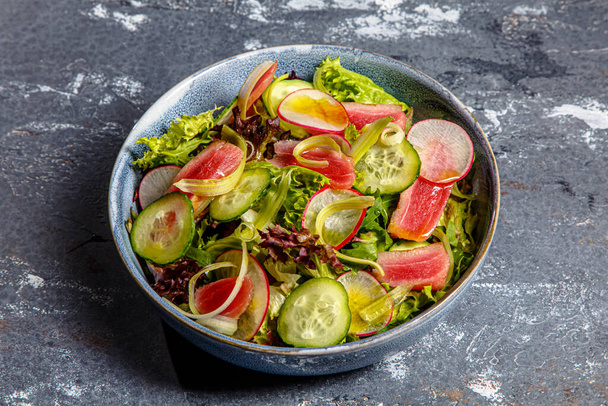Салат з листям салату, смаженим тунцем, огірками та редькою знаходиться на тарілці
 - Фото, зображення