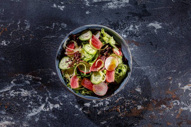Салат з листям салату, смаженим тунцем, огірками та редькою знаходиться на тарілці
 - Фото, зображення