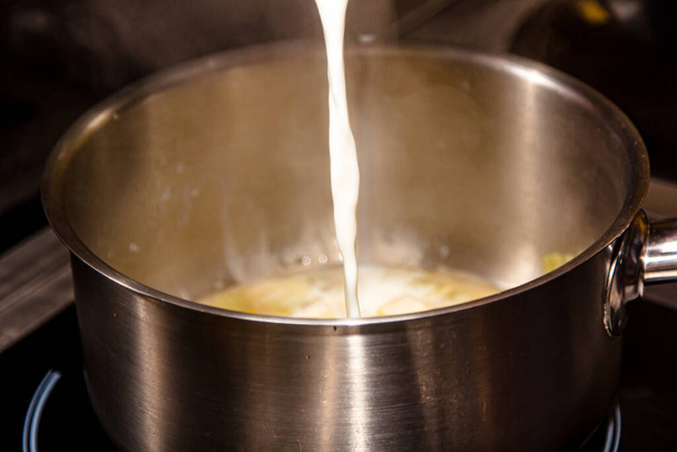 Cooking dishes from milk. Milk is poured in a trickle into a saucepan. - Photo, image