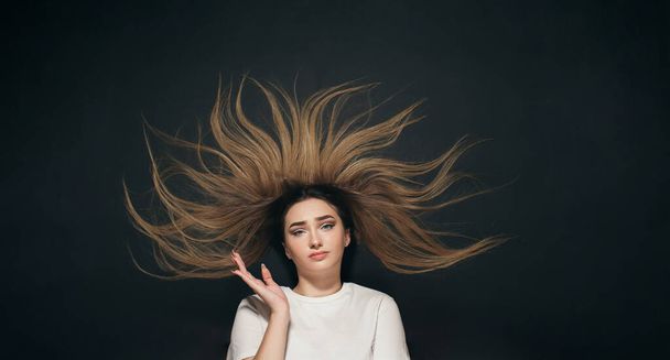 young confused woman with long hair, student on black studio background of black school board top view - 写真・画像