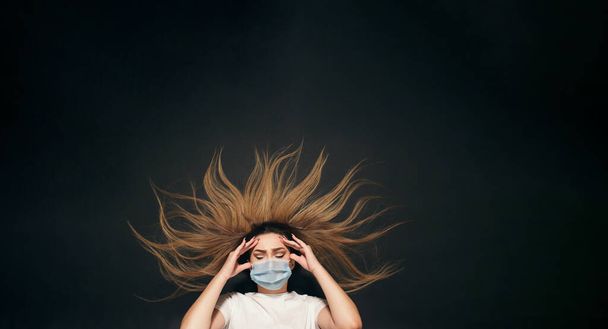 young woman in protective medical mask on her face on black studio background top view,girl grabbed her head in stress - Foto, Bild
