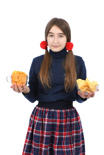 Pre-adolescent meisje weegt twee kommen vol chips. Geïsoleerd op witte achtergrond. Hoge resolutie foto. Volledige velddiepte. - Foto, afbeelding