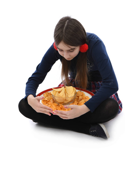 Vorpubertierendes Mädchen hält Teller voller Kartoffelchips in der Hand. Vereinzelt auf weißem Hintergrund. Foto in hoher Auflösung. Volle Schärfentiefe. - Foto, Bild