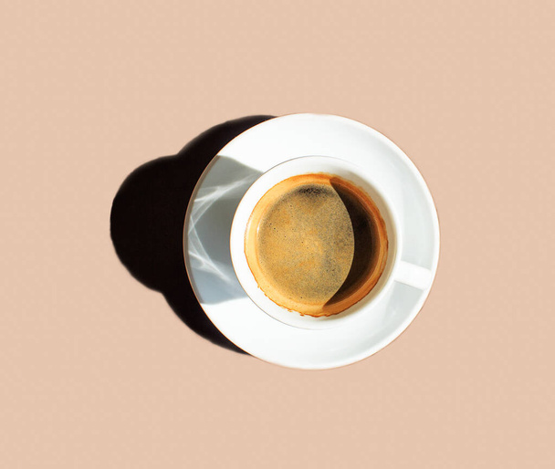 White cup of coffee with a saucer on a beige background with hard shadows. Copy space - Photo, Image