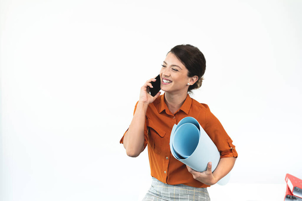 Happy businesswoman holding blueprint while talking on mobile phone  - Photo, image