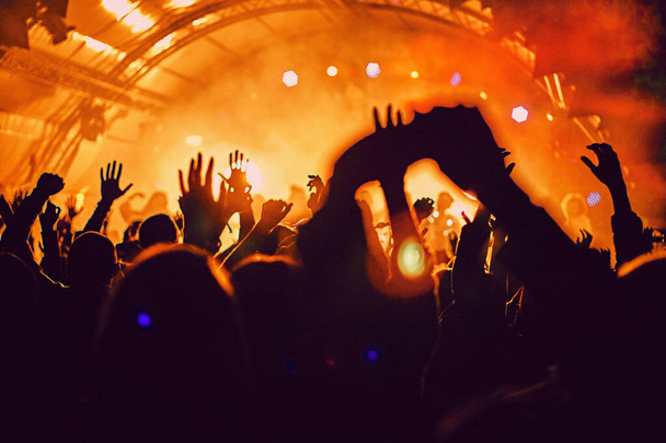 Atmosphère floue abstraite : des gens heureux profitant d'un concert de festival de musique en plein air, levant les mains et applaudissant de plaisir, concept de vie nocturne active, jeu de lumière et d'ombre sur l'immense scène - Photo, image