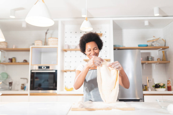 African American woman in kitchen holding rolled dough to make pizza - Foto, afbeelding