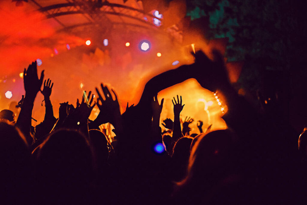 Absztrakt elmosódott atmoszféra: boldog emberek élvezik a szabadtéri zenei fesztivál koncertjét, felemelt kezekkel tapsolnak, aktív éjszakai életfelfogással, fény és árnyék játékkal a hatalmas színpadon - Fotó, kép