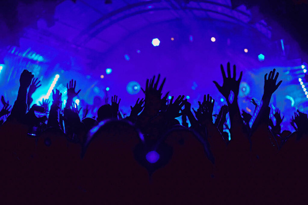 Absztrakt elmosódott atmoszféra: boldog emberek élvezik a szabadtéri zenei fesztivál koncertjét, felemelt kezekkel tapsolnak, aktív éjszakai életfelfogással, fény és árnyék játékkal a hatalmas színpadon - Fotó, kép