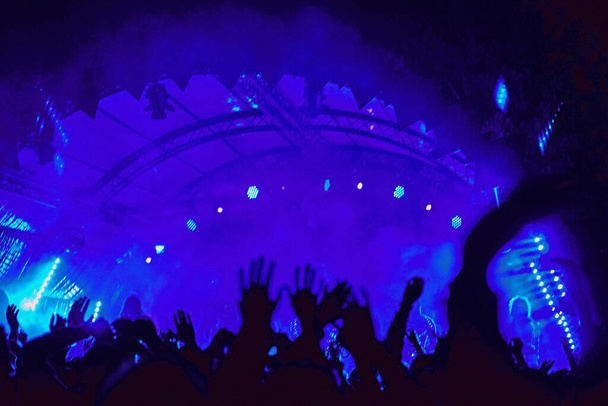 Abstract blur atmosphere: happy people enjoying outdoor music festival concert, raised up hands and clapping of pleasure, active night life concept, play of light and shadow on the huge stage - Photo, Image