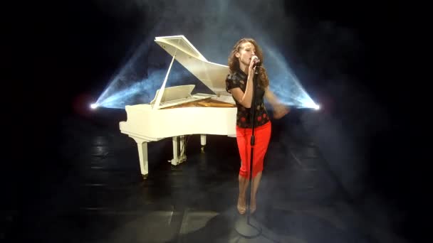 cantante femenina retro cantando jazz en el micrófono en el escenario con focos y piano blanco, música. - Imágenes, Vídeo