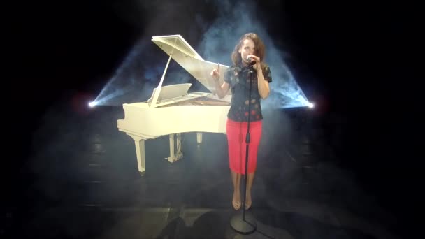retro lady cantante cantando jazz en el micrófono en el escenario con focos y piano blanco, música. - Metraje, vídeo